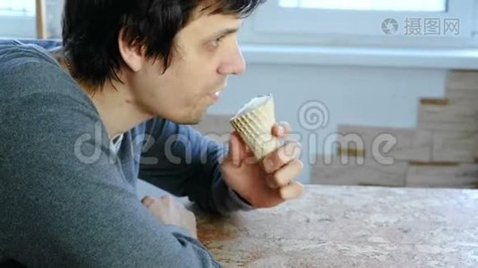 年轻人坐在窗边在家吃冰淇淋。 侧视。视频