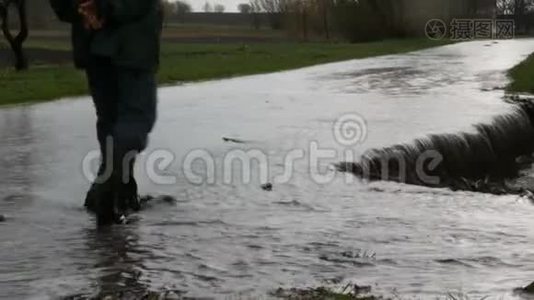 灾难。 村庄里的洪水。 肮脏的黑色河流沿着道路流动。 穿着黑色橡胶靴的人穿过视频