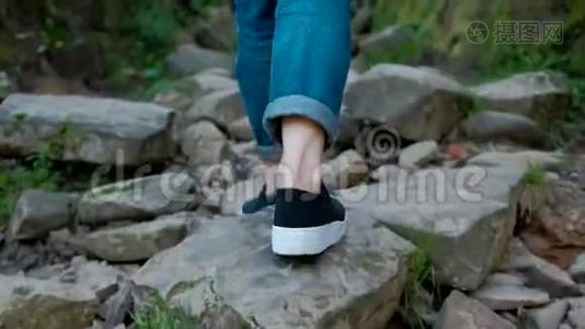 一个穿牛仔裤和交叉裤的女人的腿，独自走在一条有很多石头的山路上视频