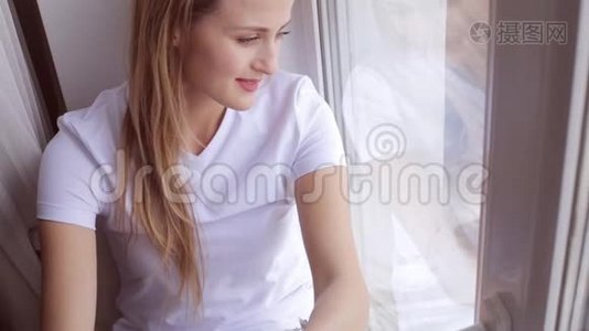 坐在窗台上的迷人梦想的年轻女子的画像视频