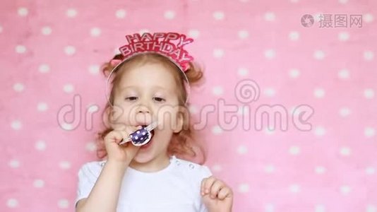 一个可爱的小女孩吹角派对，微笑，玩得开心，笑着庆祝生日快乐。 恭喜你。 特写视频
