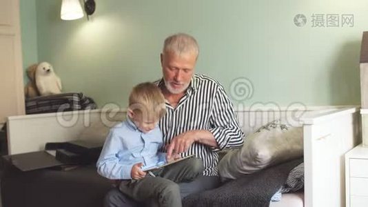 祖父和孙子坐在沙发上用数码平板电脑视频