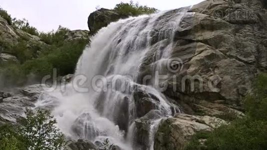 慢动作的水从一块巨大的岩石上掉下来。 阴天有小雨的自然环境中的瀑布视频