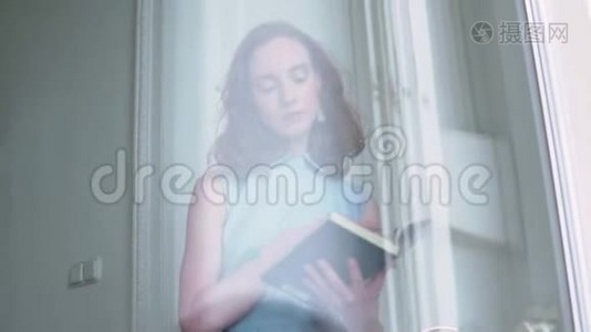 年轻的红头发女孩拿着一本书在白屋子里看书视频