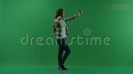 带迷你包的女孩站在她的右边，在绿色屏幕上自拍视频