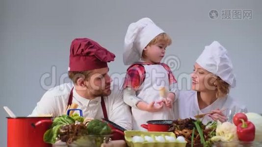 可爱的小男孩和他美丽的父母在厨房做饭时微笑。 年轻家庭在厨房做饭视频