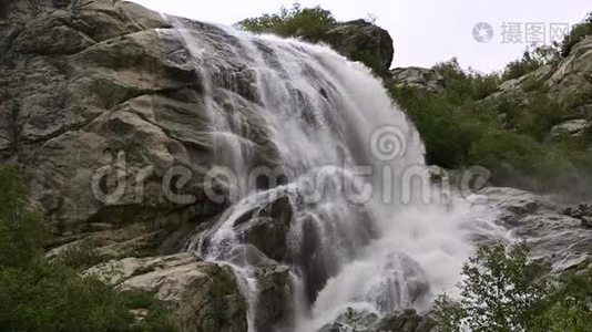 慢动作的水从一块巨大的岩石上掉下来。 阴天有小雨的自然环境中的瀑布视频