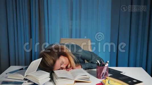 一个穿牛仔衬衫的女学生，累了，在一张有书的桌子上睡着了。视频