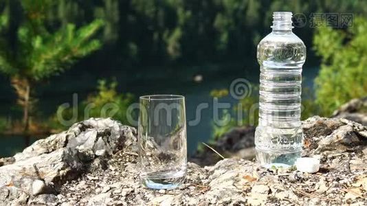 人们把干净的水从瓶子里倒入山区的玻璃里。 健康生态主题.. 慢动作视频