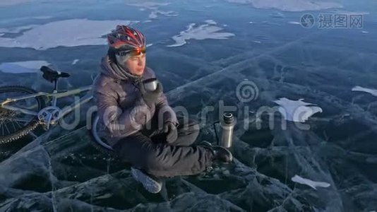 那个人正坐在冰上自行车的轮子上休息。 他喝热水瓶里的茶。 骑自行车的人穿着视频