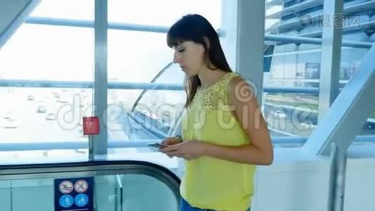 女孩站在地铁道口的自动人行道上，用智能手机说话。 在她身后的窗户上视频