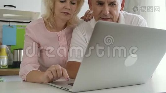 成熟的家庭夫妻在厨房里使用笔记本电脑。视频