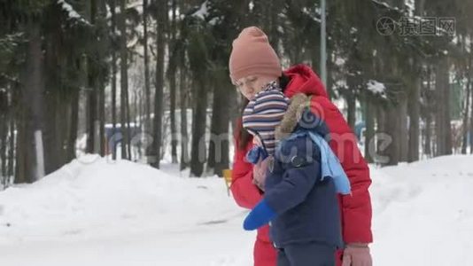 可爱的小男孩和年轻的母亲在冬天和公园里的雪玩耍。 蓝色的孩子`夹克和红色的妈妈。视频