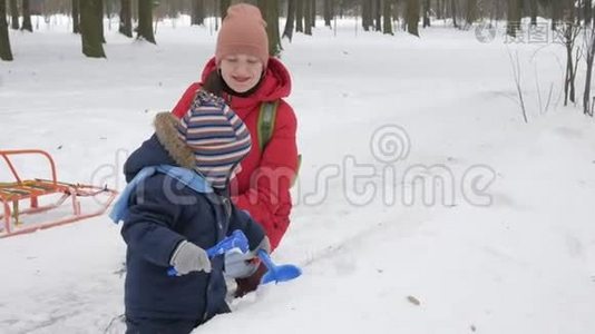 可爱的小男孩和年轻的母亲在冬天和公园里的雪玩耍。 蓝色的孩子`夹克和红色的妈妈。视频