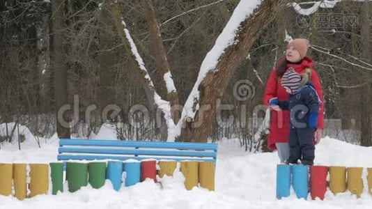 可爱的小男孩和年轻的母亲在冬天和公园里的雪玩耍。 蓝色的孩子`夹克和红色的妈妈。视频