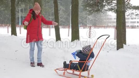 可爱的小男孩和年轻的母亲在冬天和公园里的雪玩耍。 蓝色的孩子`夹克和红色的妈妈。视频