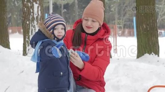 可爱的小男孩和年轻的母亲在冬天和公园里的雪玩耍。 蓝色的孩子`夹克和红色的妈妈。视频