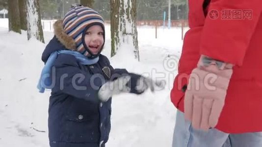 可爱的小男孩和年轻的母亲在冬天和公园里的雪玩耍。 蓝色的孩子`夹克和红色的妈妈。视频