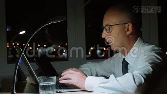行政商人在黑暗的办公室加班时使用笔记本电脑视频