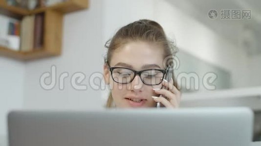 学生女孩说着手机，微笑着在家用笔记本电脑，在社交网络上聊天视频