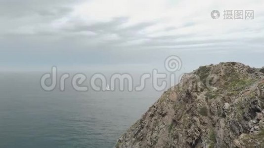 一艘孤独的游艇在海上航行，前景是巨大的岩石视频