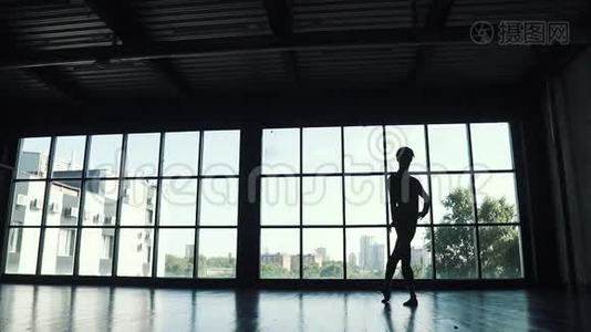 一位芭蕾舞演员的剪影，男演员在一扇大窗户的背景下跳舞。 舞蹈演员优雅地在舞蹈中翩翩起舞视频