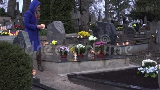 悲伤的女人坐在墓地的坟墓上，手里拿着燃烧的蜡烛祈祷。 4K视频