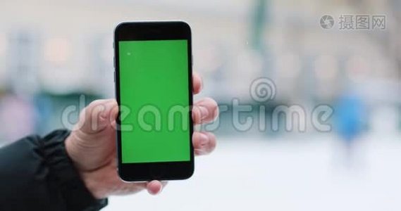 雪落在一个男人身上`他手里拿着智能手机，手里拿着绿色的屏幕视频