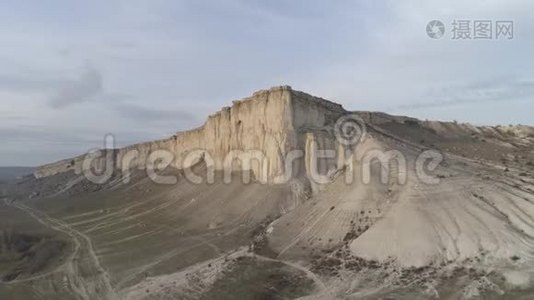 从底部看绿色低地附近的一座高灰色山脉和蓝天上的道路。 中枪。 郊野山视频