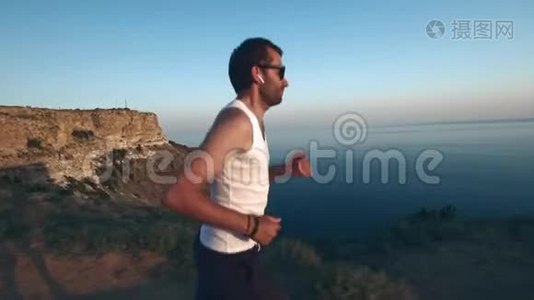 运动帅哥正在用手机和耳机做运动，在日落时沿着海岸跑步，然后慢跑视频