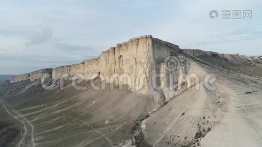 从底部看绿色低地附近的一座高灰色山脉和蓝天上的道路。 中枪。 郊野山视频