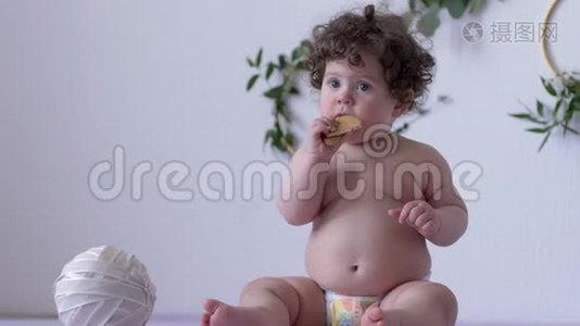 漂亮的、丰满的、卷发的小孩在室内以装饰为背景的墙上吃饼干视频