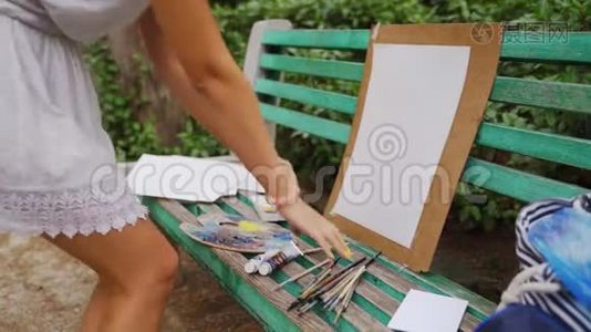 女孩艺术家准备纸调色板和油漆刷在公园的风景画与一个小池塘4k视频