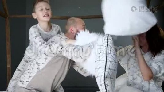 父母带着一个孩子在卧室里穿着相同的睡衣，抱着枕头在床上胡闹视频