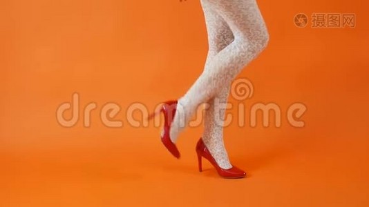 美丽的女性腿，红色高跟鞋和白色鱼网袜在橙色背景。 复古风格视频