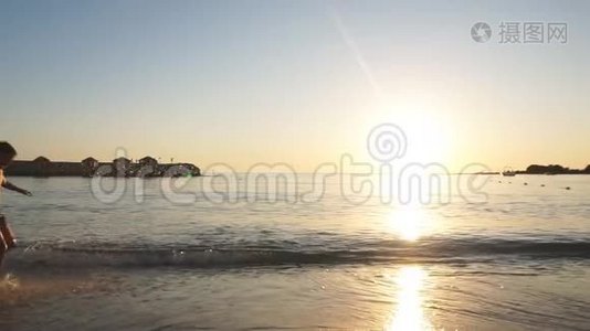日落时快乐的孩子在沙滩上奔跑的剪影。慢动作。视频