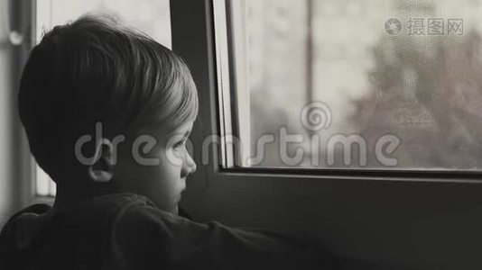 孩子悲伤而孤独地透过窗户看。 孩子沮丧的黑白镜头视频