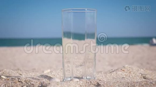玻璃矗立在沙滩上，装满饮用水，背景是大海。 特写视频
