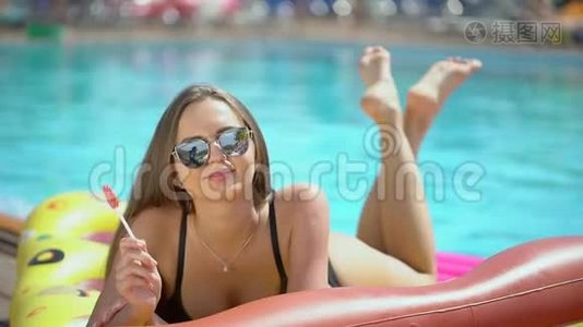 年轻女子20多岁，在暑假在游泳池附近放松。 比基尼女孩日光浴躺在充气床垫上视频