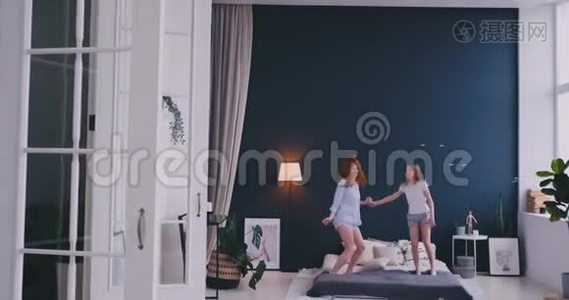幸福的家庭，可爱的女儿和年轻的母亲在床上跳跃和跳舞，而在假日的早晨玩得开心。视频