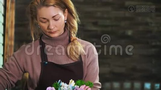一个穿着围裙的女花匠，站在一家花店的柜台上，准备一束花。视频
