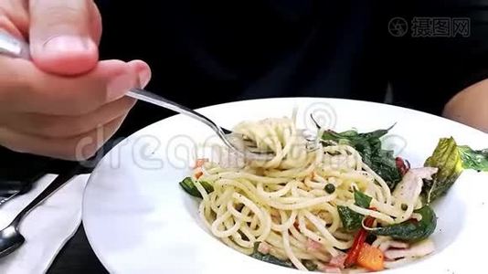 男人`手捻叉子，在桌子上白色背景上吃辛辣的意大利面。视频