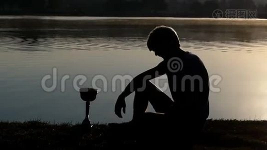 活泼的男人坐在湖岸上，望着一个邋遢的赢家碗视频