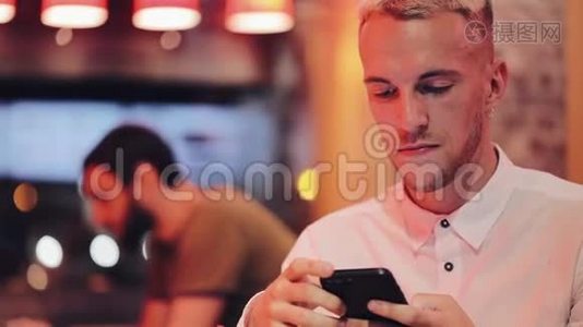 年轻英俊的男人在夜间咖啡馆里拨打电话并在智能手机上交谈。 他坐在霓虹灯旁边视频