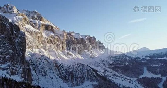 沿着白雪皑皑的高山陡峭的岩石悬崖山谷，带着森林。 日落或日出，晴空万里.. 冬季视频