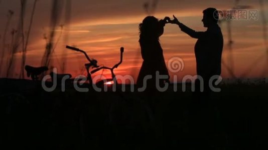 敏感的情侣在红艳艳的夕阳下在田野上跳舞。 剪影的完整视角。 步行视频