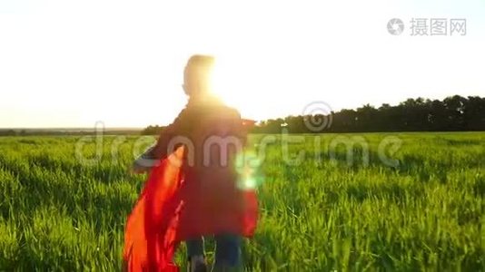 一个穿着超级英雄服装的孩子穿着红色斗篷，在日落的背景下穿过绿色的草坪。 那个男孩视频