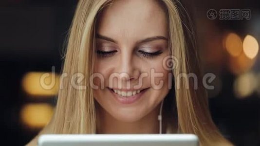 迷人的年轻女子微笑着用耳机里的平板电脑工作视频