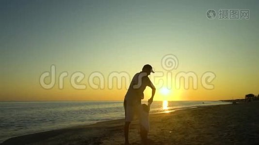 日落时，一个年轻英俊的男人和他的小女儿沿着海滨散步。 爸爸把女儿抱在怀里视频
