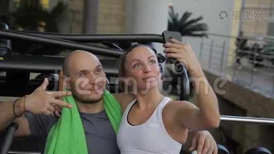 这对幸福的夫妇在健身房休息期间在全新的智能手机上自拍。视频